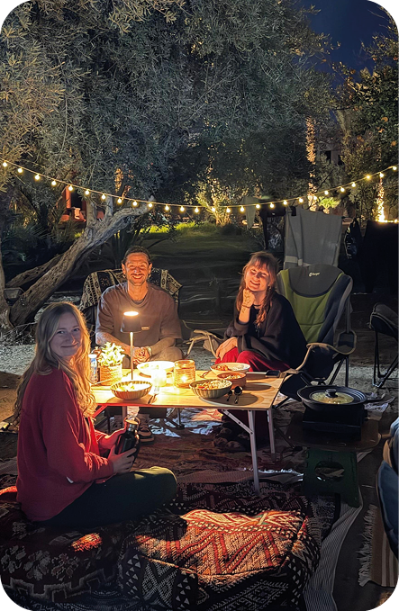 Freunde beim gemeinsamen Abendessen unter Lichterketten zwischen Olivenbäumen